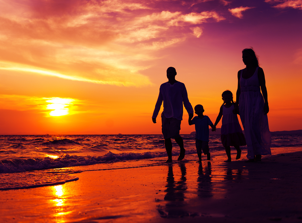 Familie steht am Strand bei Sonnenuntergang.